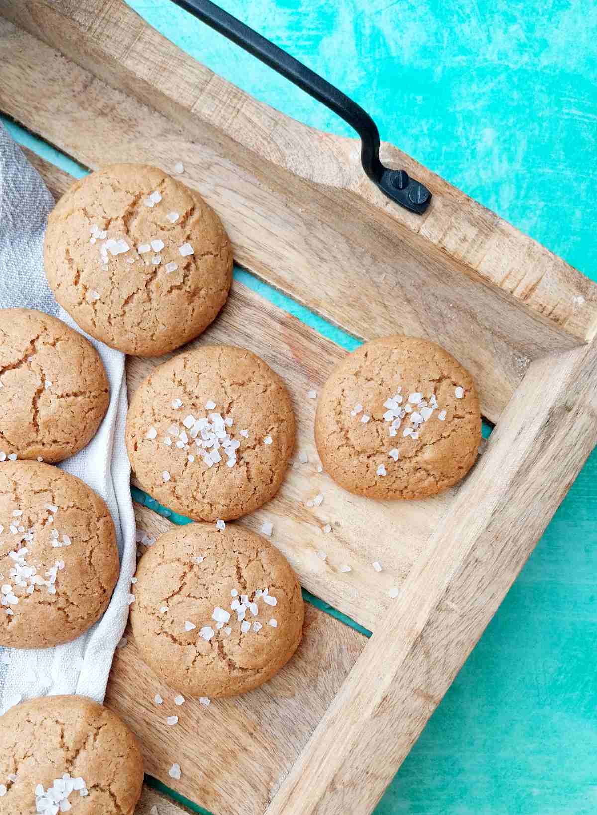 Sorghum flour cookies on a wooden tray lined with kitchen towel on a green surface.