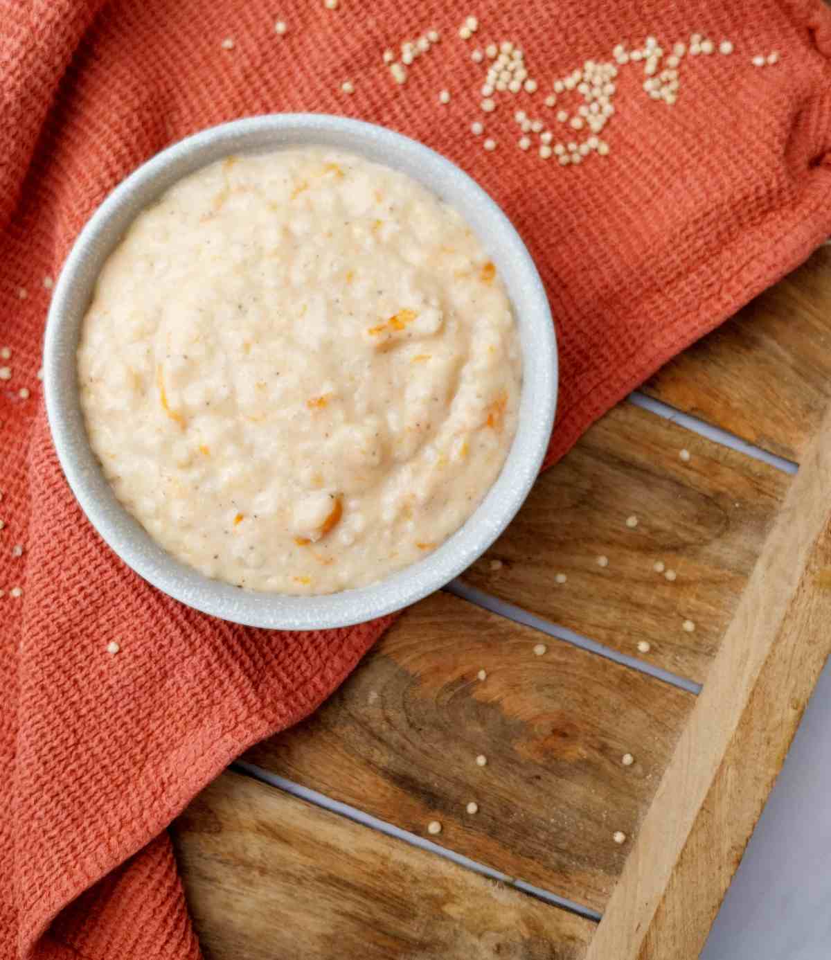 Creamy sorghum porridge in a white bowl on a wooden surface with a kitchen towel.