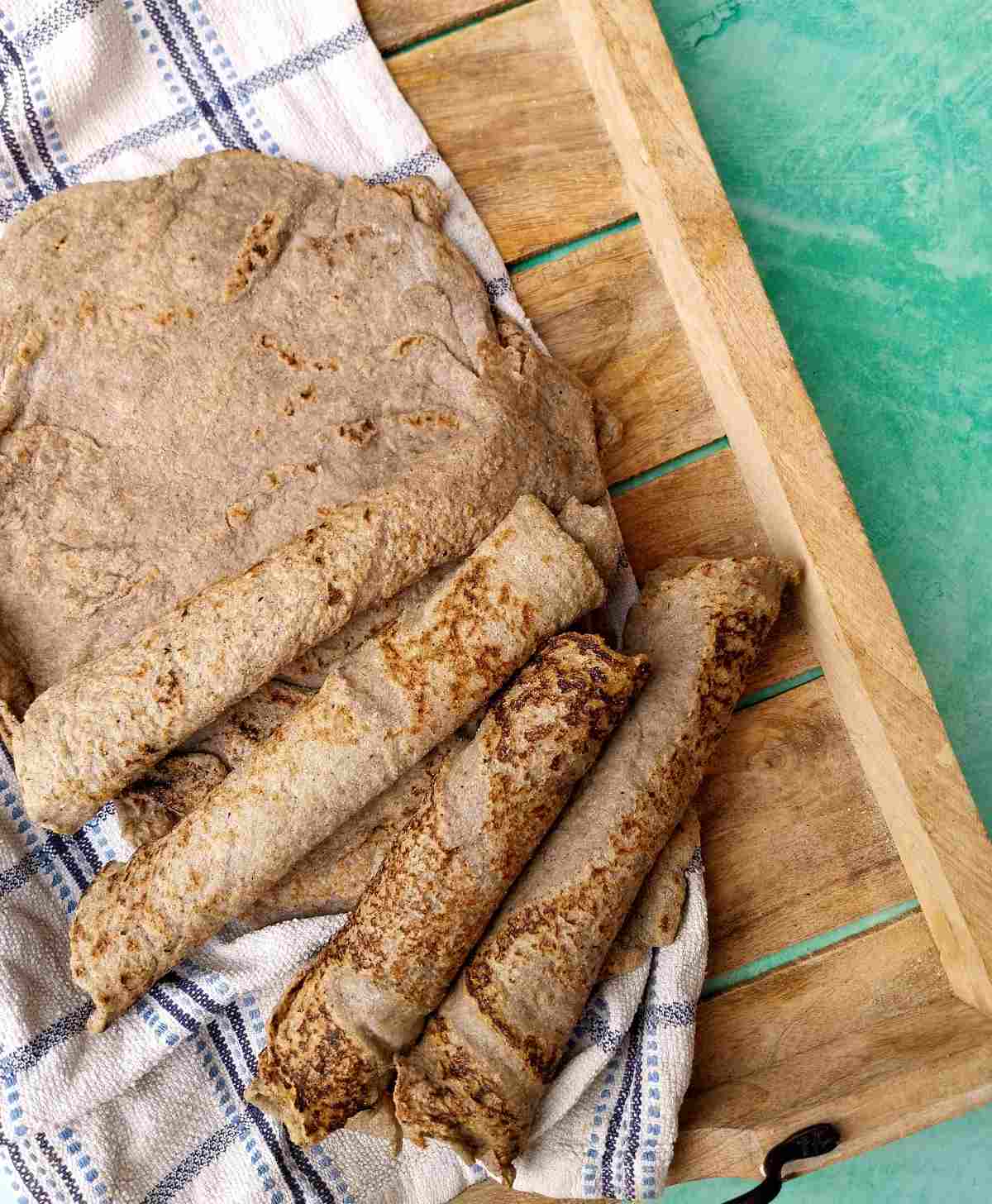 Bajra roti rolled up ona wooden tray with a kitchen towel under it on a green background.