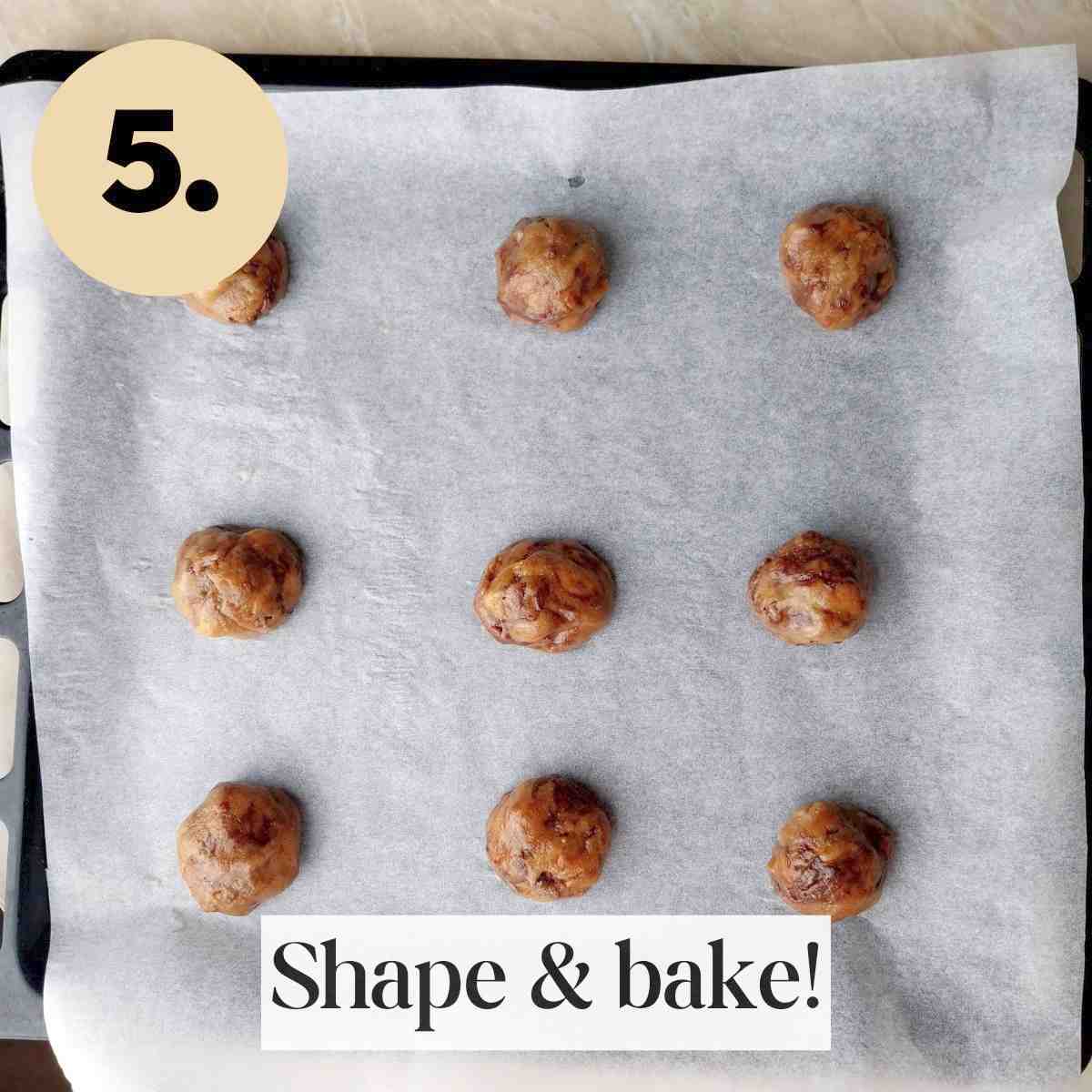 Scooped cookie dough on a white piece of baking paper on a black baking sheet.