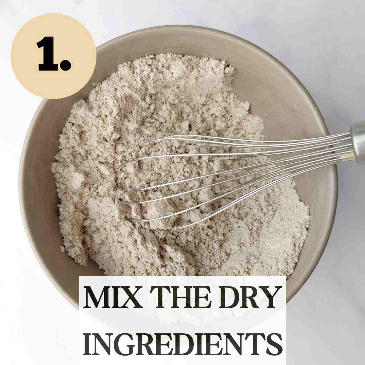 Dry ingredients for finger millet cookies in a brown bowl with a metal whisk in it on a white surface.