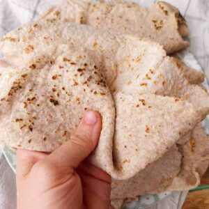 Jowar roti held in a hand with the rest of the flatbreads in hte background.