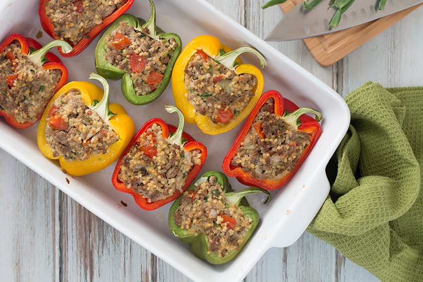 Stuffed peppers in a white casserole on a wooden surface.