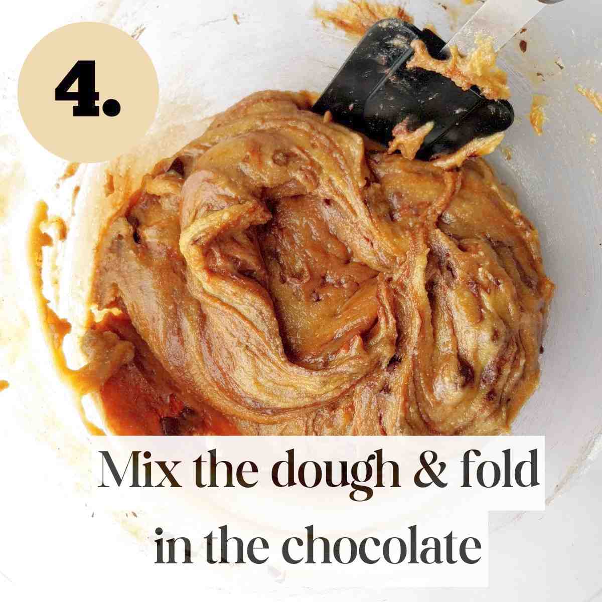 Mixed dough with a silicone spatula in it in a glass bowl against a white surface.