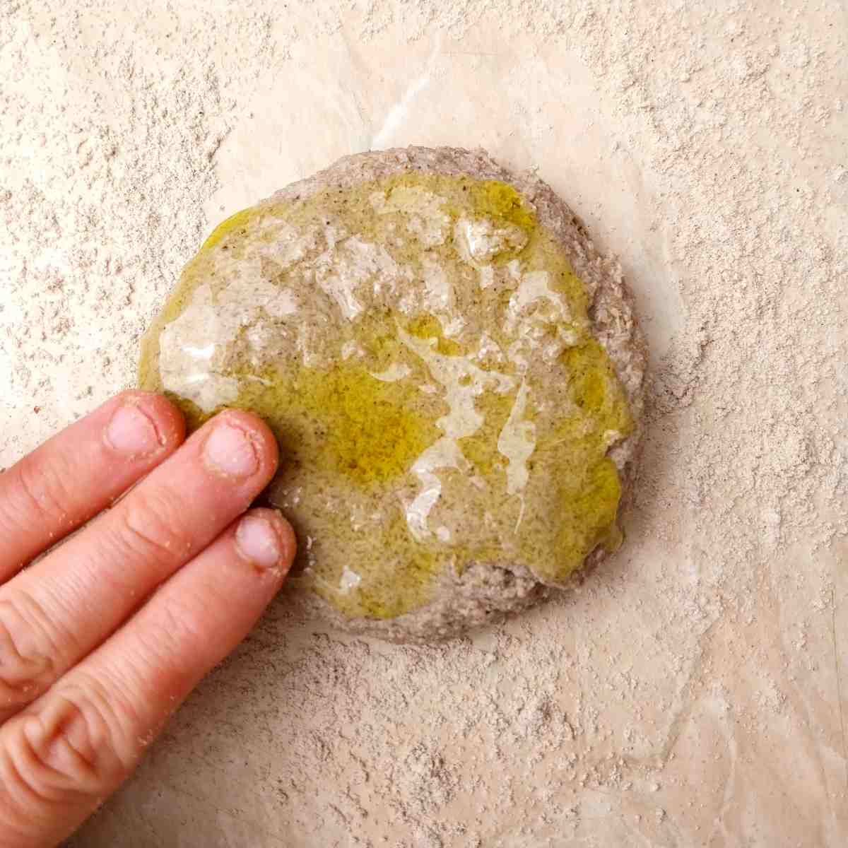 Dough ball with oil spread on it by hand against a light surface.