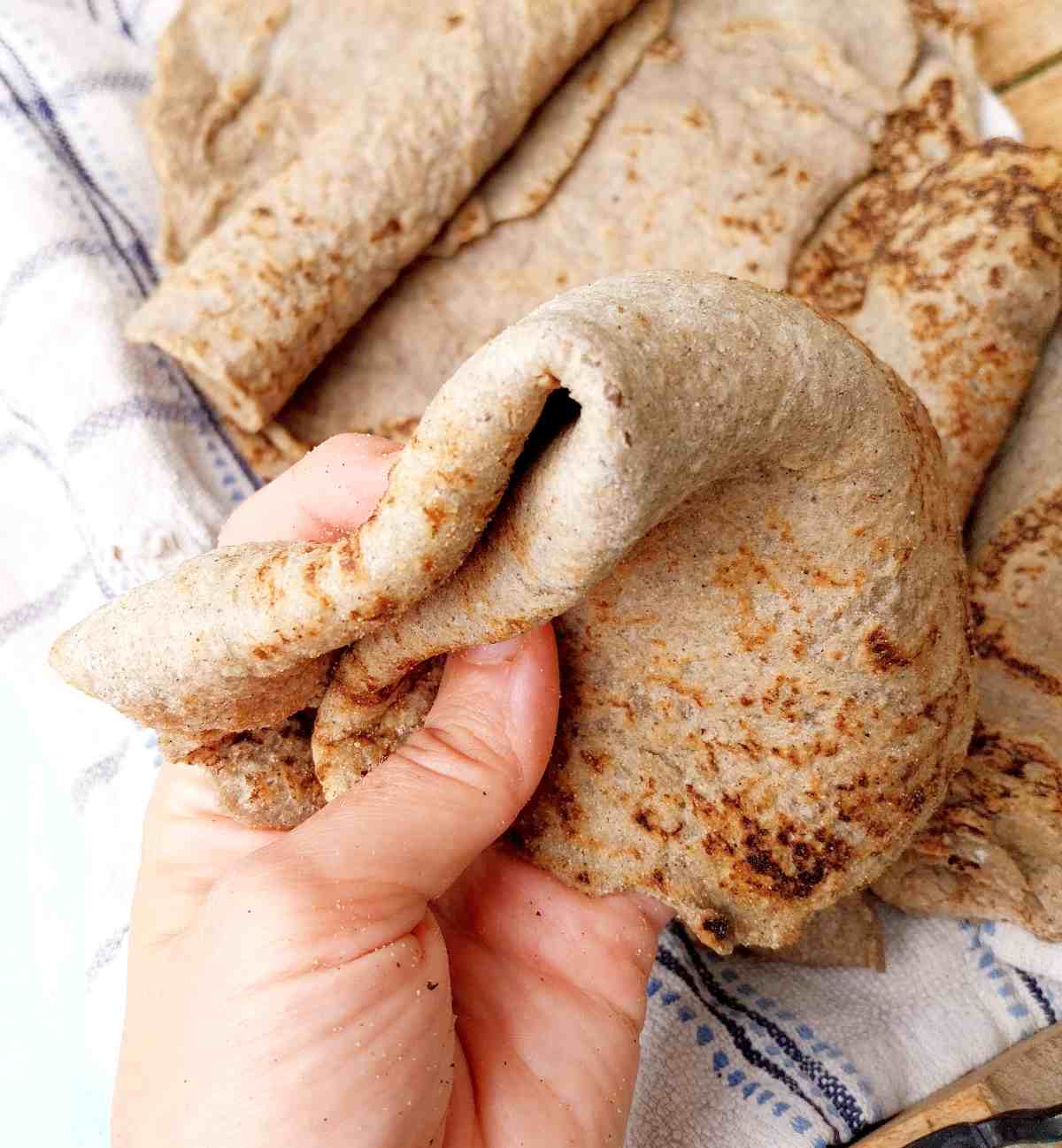 Ragi roti bent and held in a hand with the rest of the rotis in the background on a light kitchen towel.