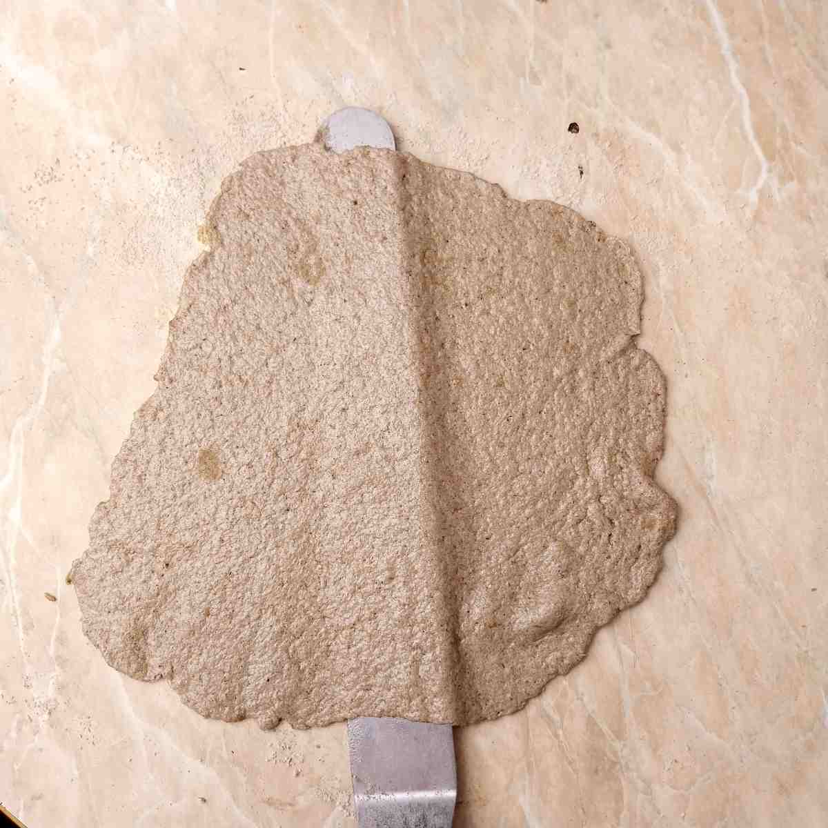 Sliding a spatula under the rolled out roti to prevent sticking.